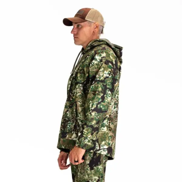 A person in profile wearing a Kryptek Tartaros Hoodie Obskura Transitional and a brown mesh-back cap stands against a plain white background. The jacket has a hood, and the individual has their hands at their sides, showcasing the side view of the outfit.