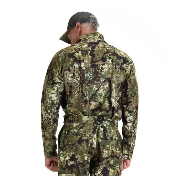 A man stands with his back to the camera, wearing a Kryptek Valhalla Long Sleeve Zip Highlander and a cap. The clothing features a mix of green, brown, and black colors, blending into a military or hunting-style pattern. The background is plain white.