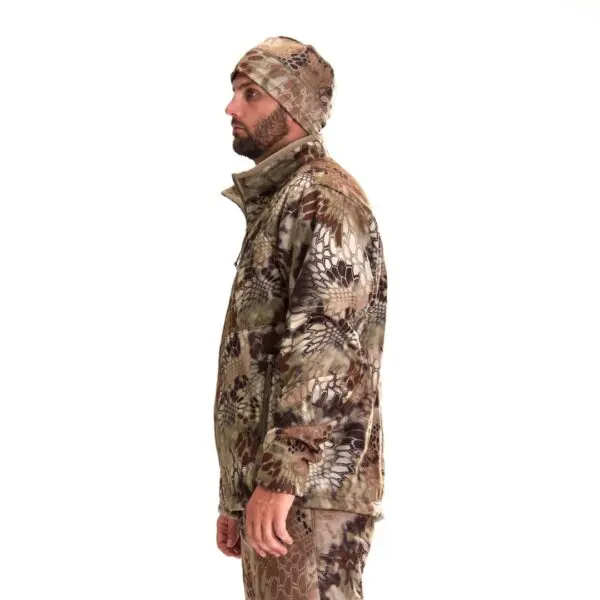 A man dressed in a full camouflage outfit stands in profile against a plain white background. He is wearing a Kryptek Njord Windproof Jacket, matching pants, and a camo beanie, looking to the left.