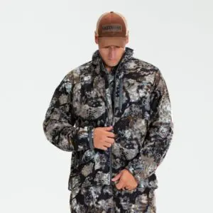 A person wearing a camouflage jacket and pants is zipping up their Kryptek Njord Windproof Jacket. They are also wearing a brown baseball cap with the word "EASTMANS" on the front. The background is plain and white.