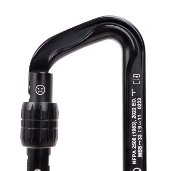 A black Omega Pacific Standard D Aluminum Keylock Screw-Lok NFPA with a locking mechanism is pictured. The carabiner has text and symbols printed on its side, including “NFPA 2500 (1983), 2022 ED.” and technical details. The locking area shows a small engraved unhappy face symbol.