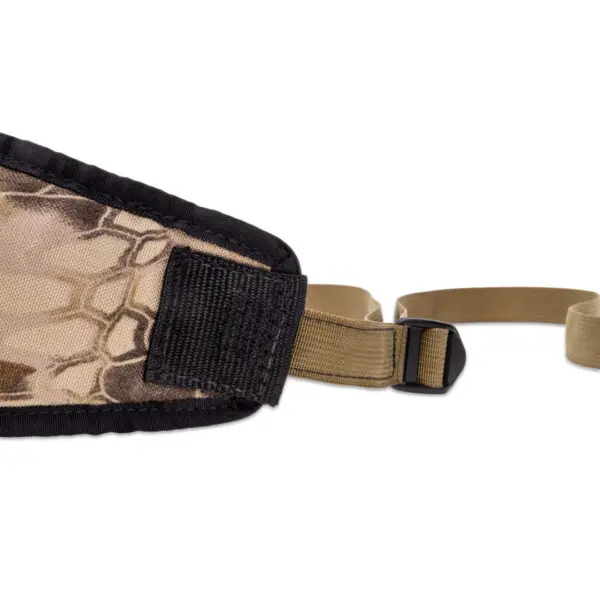 Close-up of a camouflage-patterned fabric strap. The Ape Canyon Outfitters Lazy Hunter Band Kryptek Highlander includes a black padded section and beige webbing with adjustable buckles. The design features a hexagonal honeycomb pattern in shades of brown and beige.