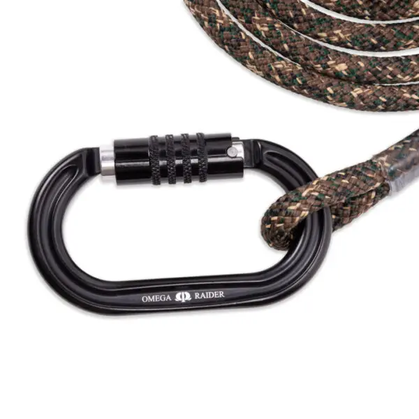 Close-up of a black Omega Raider carabiner clipped onto a brown and green braided Ape Canyon Outfitters 9.5mm Ghillie Lineman Belt Kit. The carabiner features a locking mechanism with a textured surface for better grip. The coiled rope is partially visible in the background.