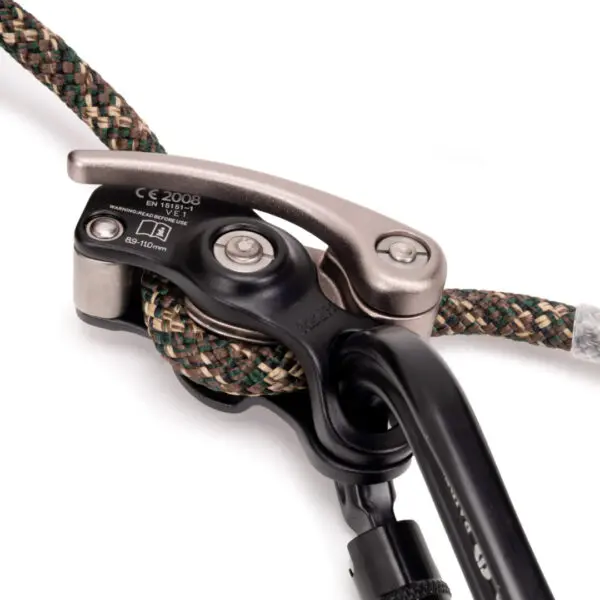 A close-up of an Ape Canyon Outfitters One Stick Rappel Kit attached to a multi-colored climbing rope. The device appears to be certified with safety standards, showing clear markings and numbers. The rope is partially visible with shades of green, beige, and black.