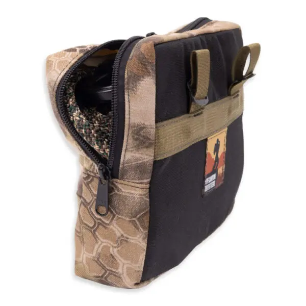 A camouflage-patterned zippered pouch with a black front panel, partially open to reveal internal contents. The Ape Canyon Outfitters One Stick Rappel Kit has two olive green attachment loops and a patch on the front featuring text and a silhouetted figure. The zipper is black with a pull tab.