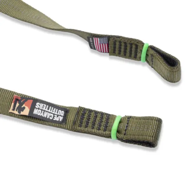 Close-up image of a green, heavy-duty strap with a black label showing a logo and the text "Ape Canyon Outfitters 3 Step Aider." There's also a small label with an American flag. The strap has reinforced stitching and a loop end secured with green rubber bands.