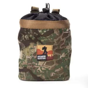 A camouflage drawstring Ape Canyon Outfitters Saddle Pouch Obskura Transitional with a tan trim and a black top. The front features a brown, red, and peach logo patch depicting a silhouette of a person photographing mountains, labeled "APE CANYON OUTFITTERS.