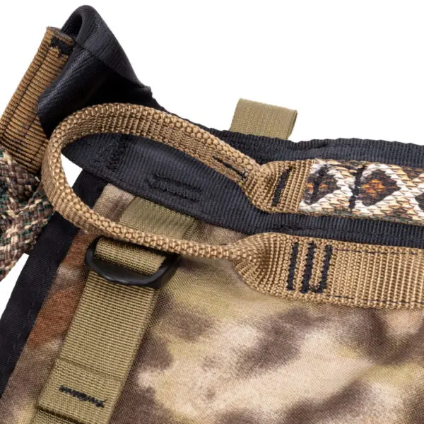 Close-up of an Ape Canyon Outfitters Pioneer Saddle Highlander strap system. The image shows a well-stitched, durable strap with webbing loops and buckles. The fabric has a camouflage pattern. One strap features a braided design, and another is looped through a black plastic D-ring.