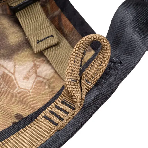 Close-up of a multicolored, camouflage-patterned Ape Canyon Outfitters Pioneer Saddle Highlander featuring various fabric straps and stitching. One prominent looped strap is stitched into the seam, with additional black and tan straps and buckles in the background.