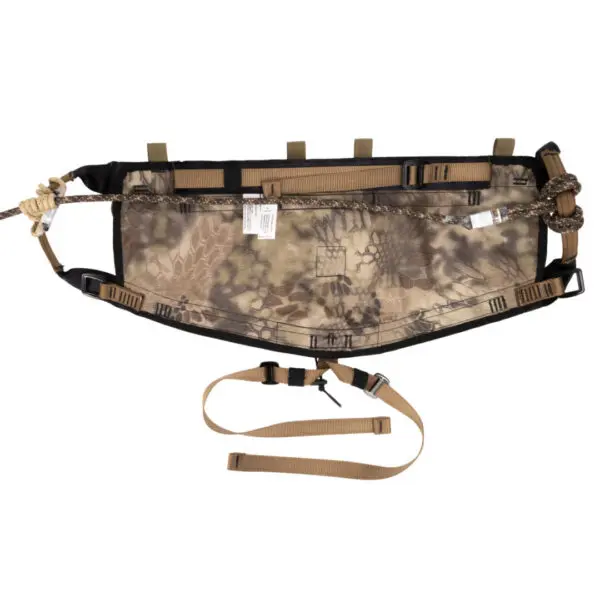 A camouflage-patterned tactical accessory belt with multiple attachment points, adjustable straps, and buckles. The Ape Canyon Outfitters Pioneer Saddle Highlander features a mix of tan, beige, and brown colors, and includes a dangling strap with a buckle for securing or adjusting the fit.