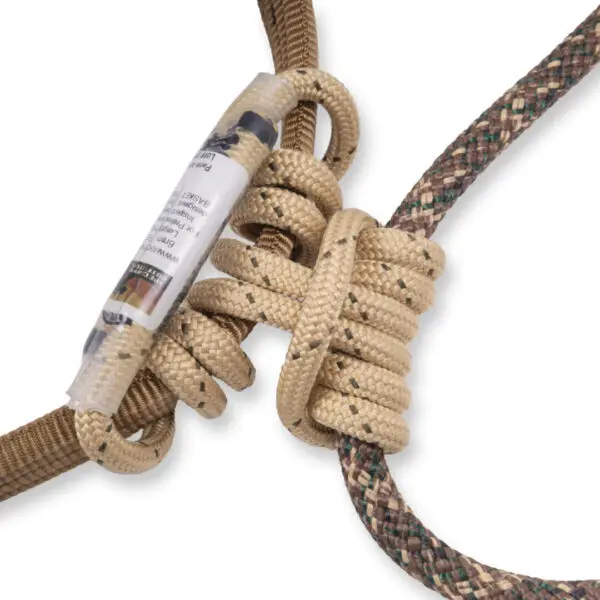 Two ropes are intertwined using a friction hitch knot. One rope is beige with black specks, and the other is a mix of green and brown. A label is attached to the beige rope, displaying some text. The background is plain white.

The Ape Canyon Outfitters Pioneer Saddle Obskura Skyfall With Cobra Pro Style Buckles is prominently featured in the image.
