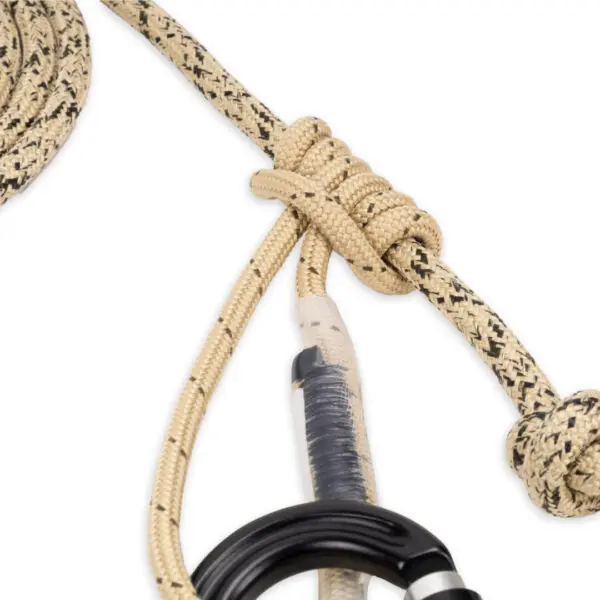 A close-up of a beige and black cord tied in a secure, intricate knot. The cord is used for climbing or rigging. A metal Ape Canyon Outfitters 8mm Resc Tech Lineman Belt with 3 Stage Quick Lock Carabiners with a black and silver design is attached to the cord at the knot, emphasizing the setup's strength and reliability.