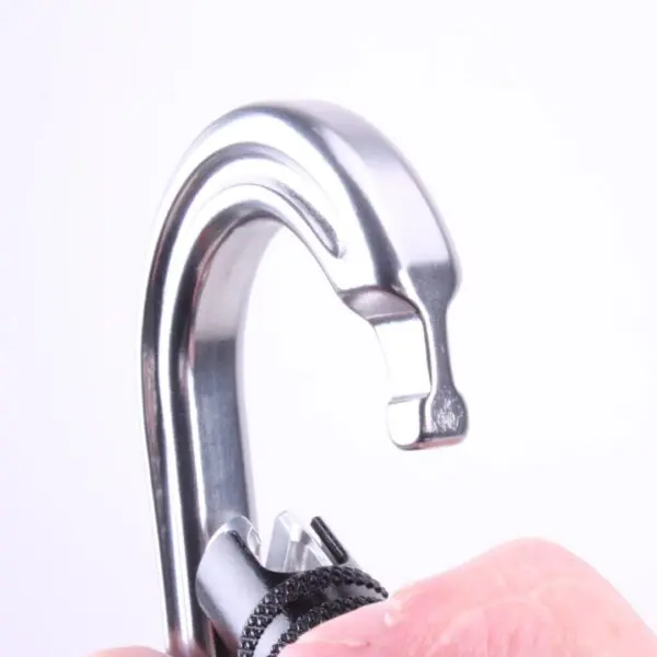 A close-up image of a metallic hook-shaped device with a polished, silver finish. The hook is being held by a person, whose fingers are visible, and is attached to an Omega Pacific Raider Aluminum Keylock 3-Stage Quik-Lok W/Captive Eye NFPA at the bottom. The background is plain white.