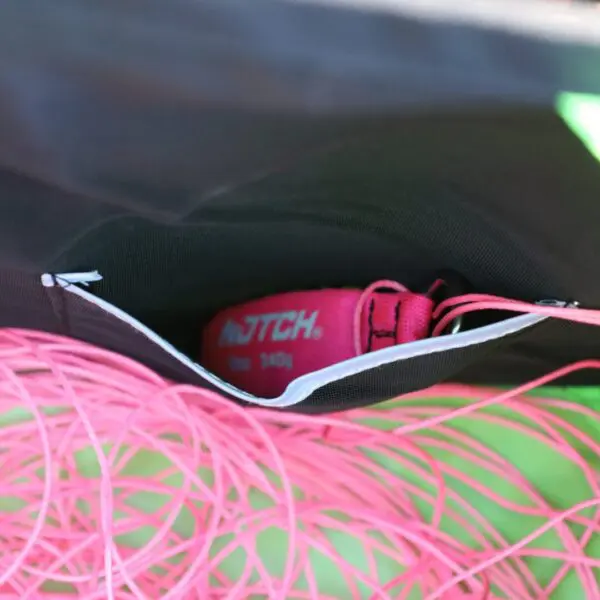 A close-up view of a RNA COLLAPSIBLE THROWLINE CUBE nestled inside a dark bag with a pink rope coiled in the foreground, suggesting preparation for a climbing or rappelling adventure.