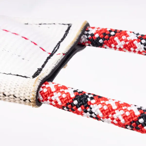 Close-up image of a Hound Hose Dog Tug Toy with two red, black, and white woven ropes looped through. The ropes are intertwined in a crisscross pattern and attached to a white textile pad with black stitching. The toy appears to be used for playing or training purposes.