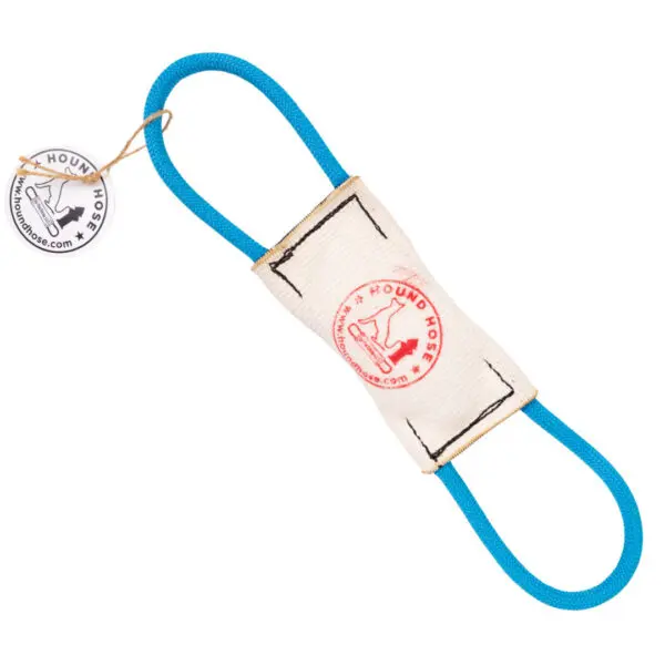 A white and light tan Hound Hose Dog Tug Toy with blue rope handles on both ends. The toy has a rectangular cloth center with a red circular logo that features a dog image and reads "Hound Hose." A round tag is attached to the toy with the Hound Hose logo.