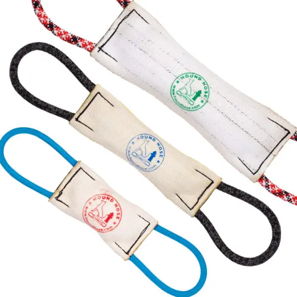 Three Hound Hose Dog Tug Toys are shown against a white background. Each toy has a cylindrical, fabric body with looped handles at both ends. They are color-coded with different loops: red and black, black, and blue. The fabric bodies have logos stamped on them.