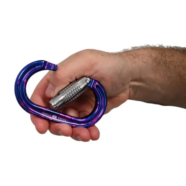 A hand holding a purple and blue gradient Omega Pacific Raider+ Aluminum Keylock 3-Stage Quik-Lok Ultra-Violet with a silver locking mechanism. The carabiner is shown from a side profile against a white background.