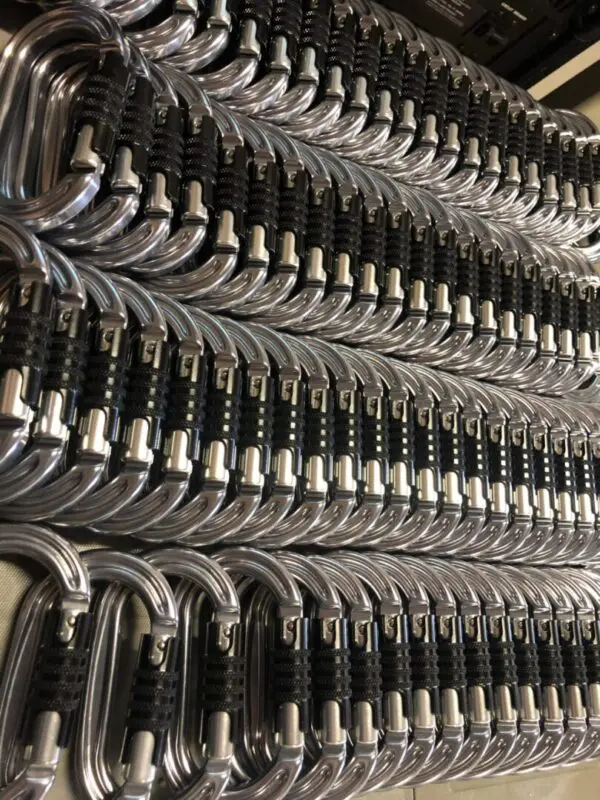 A neatly arranged row of Omega Pacific Raider Aluminum Keylock 3-Stage Quik-Lok W/Captive Eye NFPA with black webbing, lined up in a parallel formation. The carabiners are identical and appear to be new, ready for use in climbing or other activities requiring secure fastening.