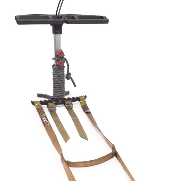A black and gray metal device with a flat, rectangular platform and a vertical support pole, featuring two brown adjustable straps with buckle attachments. The pole has a coiled rope and two red adjustment knobs. The setup is placed on a white background is the Ape Canyon Outfitters Loaded Prospector One Stick.