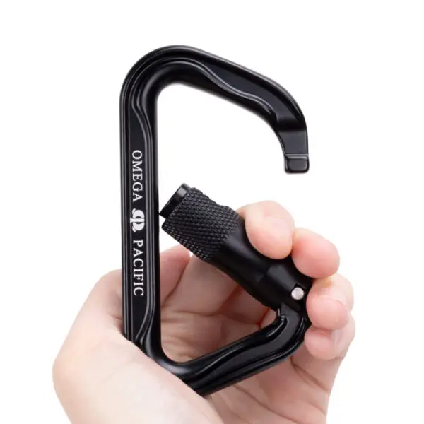 A hand is holding a black Omega Pacific Standard D Aluminum Keylock 3-Stage Quik-lok NFPA with a screw-lock mechanism. The carabiner is partially open, and the brand name "OMEGA PACIFIC" is visible on its side. The hand grips the carabiner, showcasing its size and functionality.