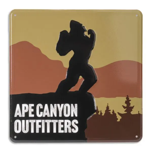 A square sign with a sunset background showing a silhouette of Bigfoot on a rocky cliff. Trees and mountains are in the distance. The text at the bottom reads "Ape Canyon Outfitters Vintage Metal Sign" in bold white letters.
