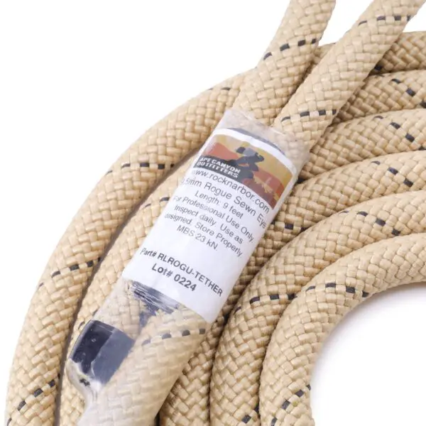Close-up of a beige and black braided rope with a label. The label contains text indicating specifications, including diameter, length, usage type, inspection requirements, and product details such as part number and lot number of the Ape Canyon Outfitters 9.5mm Rogue Tether.