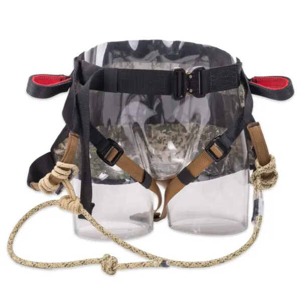 A transparent plastic saddle with straps, designed as a donkey saddlebag. The Ape Canyon Outfitters Wood Deluxe Saddle Obskura Transitional features black straps with plastic buckles, brown and beige rope handles, and red accents on the ends of the straps.