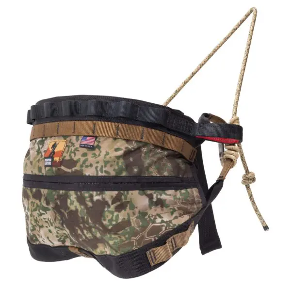An Ape Canyon Outfitters Wood Deluxe Saddle Obskura Transitional with a sturdy rope attached for safety and control. The harness features an American flag patch and additional patches, and it has adjustable straps and secure buckles for a comfortable fit.