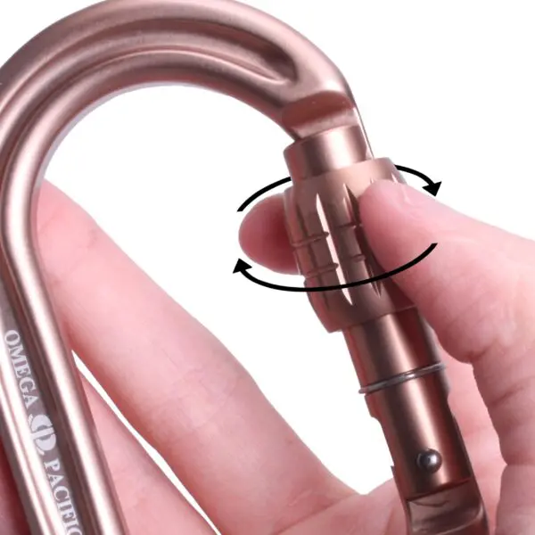 A hand is shown operating a bronze-colored carabiner. The person's fingers are rotating a screw gate lock mechanism on the carabiner. The text “Omega Pacific Raider Tactical Oval Screw-Lok Sand Tan” is visible on the carabiner's side. Arrows indicate the direction of the rotation.