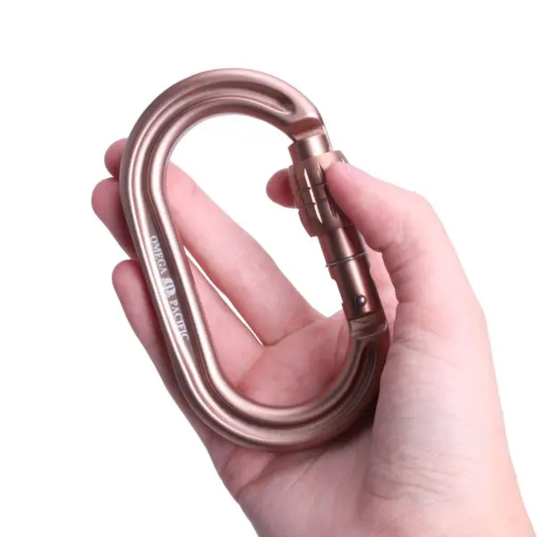 A hand holding a large, bronze-colored carabiner with a screw lock mechanism. The carabiner is oval-shaped and has the brand name "Omega Pacific Raider Tactical Oval Screw-Lok Sand Tan" printed on it.