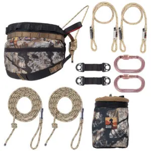 An Ape Canyon Outfitters Wood Deluxe Saddle Kit Skyfall including a padded saddle, two lineman's ropes, two carabiners, a gear pouch, and bridge straps. The saddle, pouch, and ropes feature a camo pattern for concealment in wilderness environments.