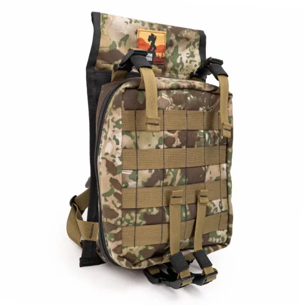 An Ape Canyon Outfitters Canyon Quiver Highlander with MOLLE webbing on the front and sides. The main compartment has black zippers, and there is a small patch with an orange and brown design at the top. The backpack has black and tan straps for securing items and carrying.