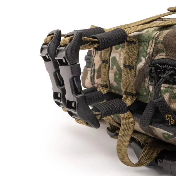 Close-up image of an Ape Canyon Outfitters Canyon Quiver Highlander showing two black plastic buckles and webbing straps. The fabric features a green, brown, and beige camo pattern, and there's a small logo of a lion sewn near the zipper on the right.