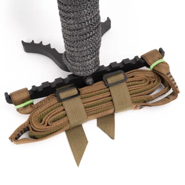 A close-up view of the Scout One Stick reveals a wrapped brown rope secured by green bands and brown straps, all attached to a black, textured grip. The black component features serrated edges and includes a mounting bracket.