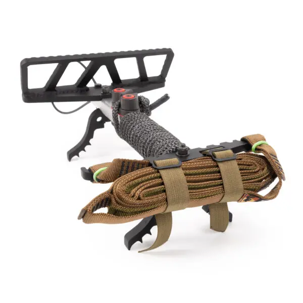 The Scout One Stick is a tactical survival tool featuring a black metal saw-toothed handle, a textured grip, and a wrapped paracord. It includes a brown sheathed multi-tool attached with tan straps for compact and easy carrying, making it ideal for outdoor or emergency use.