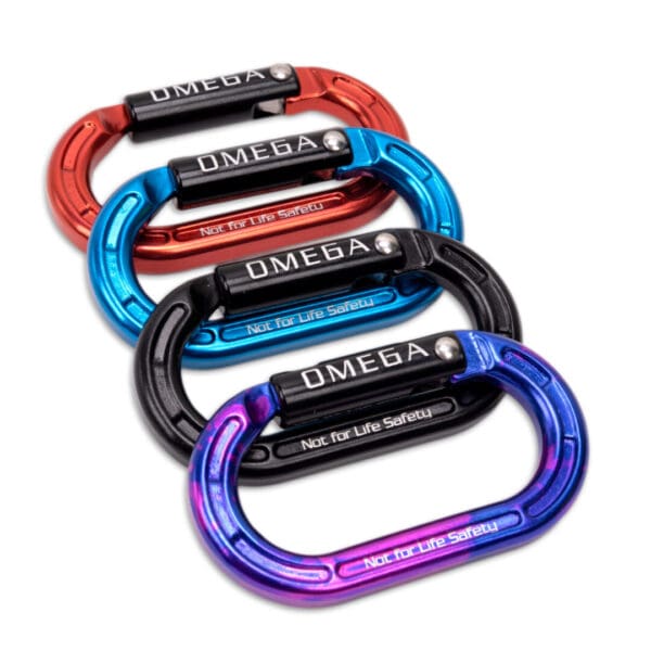 Four colorful Omega Pacific Micro Raider Aluminum Keylock Straightgates are arranged in a staggered stack. From top to bottom, the colors are red, blue, black, and a multi-colored iridescent finish. Each Omega Pacific Micro Raider Aluminum Keylock Straightgate has the word "OMEGA" and the warning "Not for Life Safety" printed on them.