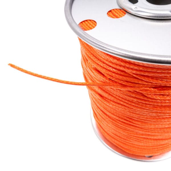 A close-up image of a spool of bright orange Ape Canyon Outfitters 2.2mm Orange Oasis synthetic rope. The rope is tightly wound around the spool, with a single strand hanging loose. The spool has a metallic rim and two circular openings through which the rope can be threaded.