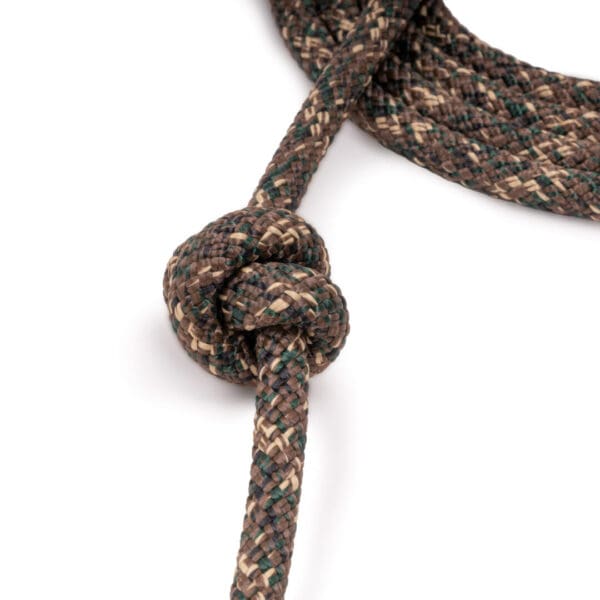 Close-up of a sturdy rope made from interwoven brown, beige, and green fibers. The Ape Canyon Outfitters 9.5mm Lineman Belt is tied into a simple, secure knot with the loose end extending out of the frame.