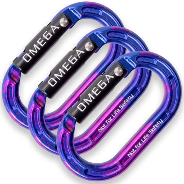 Image of three metallic carabiners with a blue and purple gradient finish. The carabiners are labeled "OMEGA PACIFIC MICRO RAIDER ALUMINUM KEYLOCK STRAIGHTGATE" in white text on the black locking mechanisms. The bottom of each carabiner is inscribed with the warning "Not for Life Safety.
