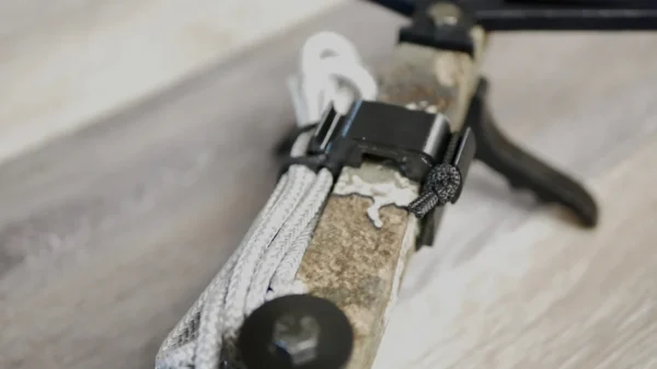 Close-up shot of a Stick Hitch & Receiver Combo attached to a rope looped through a figure-eight knot. The Stick Hitch & Receiver Combo is clipped onto a climbing anchor, secured to a rough-textured rock. The background features a blurred view of a wooden surface.