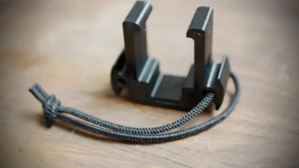 A close-up of a black Stick Hitch & Receiver Combo resting on a wooden surface. The product has two upright rectangular prongs and a knotted black string loop attached.