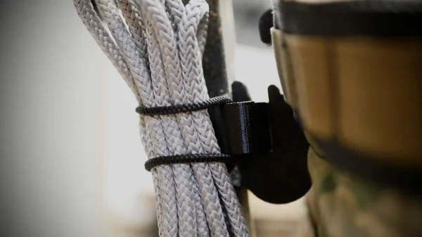 Close-up of a Stick Hitch & Receiver Combo secured with black fasteners to the side of a camouflage-patterned bag. The image is focused on the texture and details of the Stick Hitch & Receiver Combo and its securing mechanism.