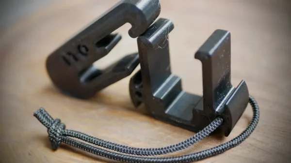 Close-up of a Stick Hitch & Receiver Combo with a small black cord attached, resting on a wooden surface. The combo has a hinged design and an "110" marking on one part, and it is opened, showing its inner mechanisms and structure.