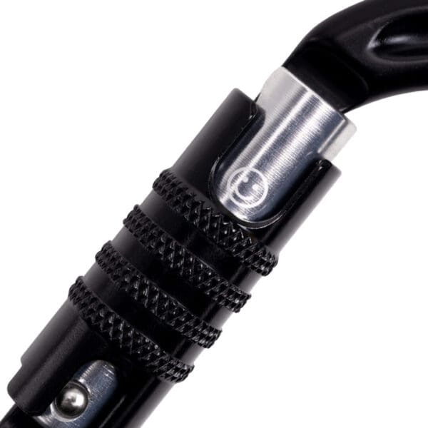 Close-up of a black Omega Pacific Raider Aluminum Keylock 3-Stage Quik-Lok NFPA - Black with a twist lock mechanism. The twist lock has a textured surface for better grip and a small circular logo is visible in the middle of the metal part of the carabiner.