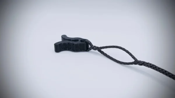 A black Flexi Ohm Tether Locker with a toggle attached to a black braided rope against a plain white background. The Flexi Ohm Tether Locker appears to be made of plastic and is designed to securely adjust the length of the cord.