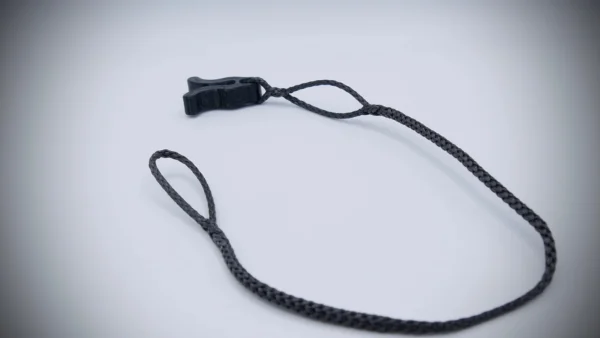 A black braided wrist strap with a small plastic buckle lies on a light gray surface. The Flexi Ohm Tether Locker has a loop at each end, with the buckle attached to one loop.