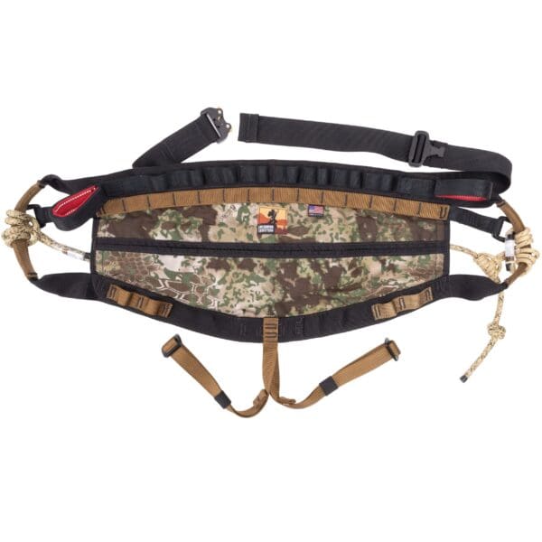 The Ape Canyon Outfitters Wood Deluxe Saddle Obskura Transitional features a camouflage-patterned tactical waist belt with adjustable black straps and multiple attachment points. It includes zippered compartments, buckles, and tan fabric loops with various fastening mechanisms.